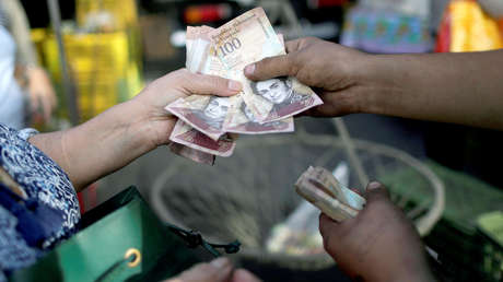 Un cajero recibe billetes bolívares venezolanos de un cliente en un mercado callejero en el centro de Caracas, Venezuela.