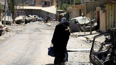 Una mujer desplazada camina con un niño en sus brazos, Mosul, Irak.