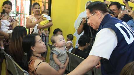 Philippines Health Secretary Francisco T. Duque III talks to a woman with a baby.