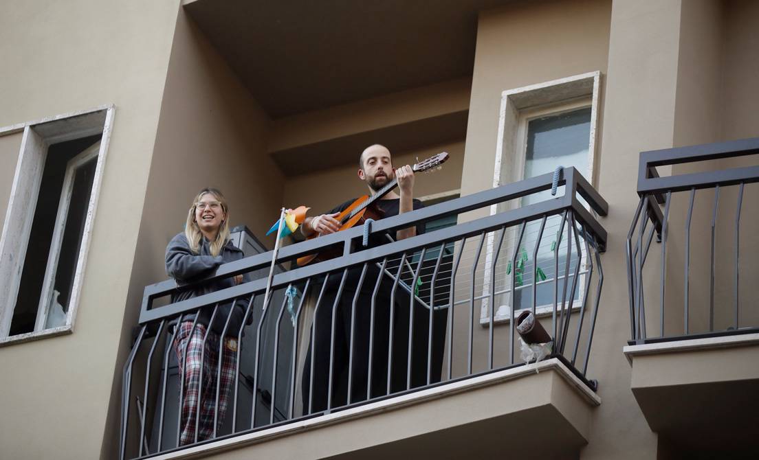 Un hombre toca la guitarra en el balcón de su casa en Milán (Italia), el viernes 13 de marzo de 2020.