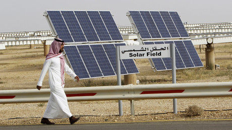 A Saudi man walks on a street past a field of solar panels © Fahad Shadeed 