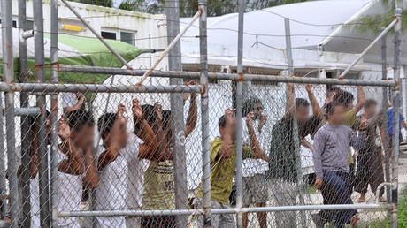 FILE PHOTO: Asylum seekers stand behind a fence in Oscar compound at the Manus Island detention centre in Papua New Guinea. © Eoin Blackwell