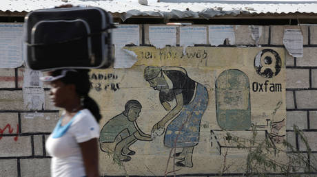FILE PHOTO. A woman walks next to an Oxfam sign in Corail, a camp for displaced people of the 2010 Haiti earthquake.