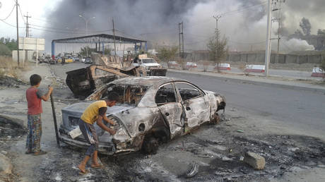 Children stand next to a burnt vehicle during clashes between Iraqi forces and ISIS in Mosul, Iraq on June 10, 2014 © Reuters / Stringer 
