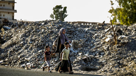 A woman and two children walk past debris in the northern Syrian city of Raqa, the former Syrian capital of the Islamic State (IS) group, on August 21, 2019. © AFP / Delil SOULEIMAN