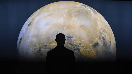 A person is seen against a projection of the planet Mars.