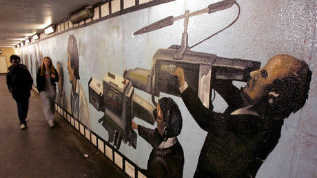 Pedestrians pass a mural showing camera operators in an underpass beside the BBC's main offices
