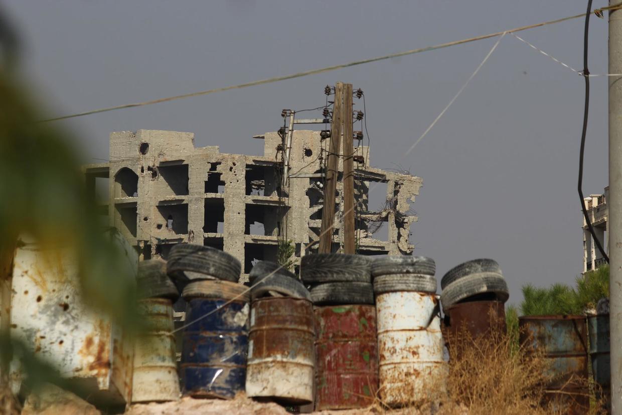 An Al-Nusra Front military building looms above the metal barrels that protect civilian neighborhoods from sniper fire. Al Zahraa, west Aleppo. ©  Vanessa Beeley 