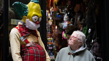 An elderly woman walks passed a Simpsons character in a surgical face mask outside a fancy dress shop on March 18, 2020 in Cardiff, UK © Getty Images / Matthew Horwood