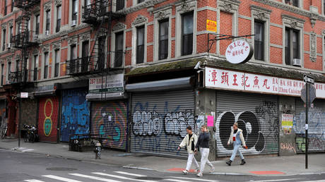 People walk by rows of shuttered stores, closed due to restrictions in place in an attempt to curb the spread of coronavirus, in the Lower East Side neighborhood of Manhattan, New York City, US