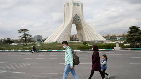 A family wear protective face masks and gloves, amid fear of Covid-19, as they walk by the iconic Freedom Square, in Tehran, Iran March 26, 2020. © Reuters / WANA / Ali Khara
