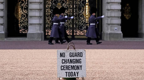 Guardsmen march behind a sign signifying no Changing of the Guard Ceremony at Buckingham Palace, London. © Getty Images / PA Images / Aaron Chown
