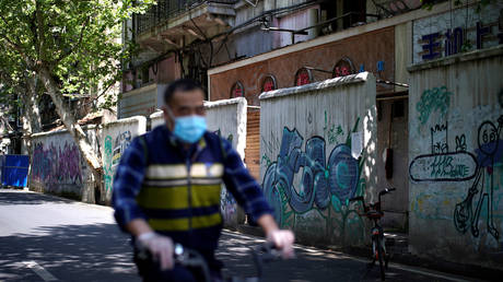 FILE PHOTO: A man wearing a face mask rides a bicycle past graffiti on walls in Wuhan, China, widely believed to be the original epicenter of the novel coronavirus outbreak.
