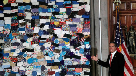 Andrew Cuomo next to mural made up of hundreds of face masks in New York