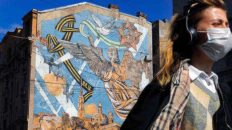 A woman wearing a face mask to protect against coronavirus walks past a graffiti dedicated to the victory of the Soviet Union in the World War II, in St.Petersburg, Russia, Monday, May 4, 2020. © AP Photo/Dmitri Lovetsky