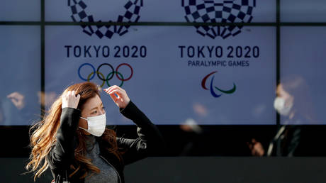 FILE PHOTO: A passerby wearing a protective face mask walks past a screen displaying logos of Tokyo 2020 Olympic and Paralympic Games in Tokyo, Japan March 19, 2020 © Reuters / Issei Kato
