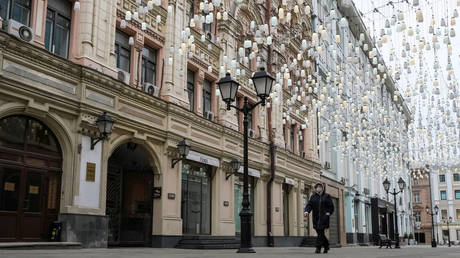 A woman wearing a protective mask walks past closed shops along a street in Moscow