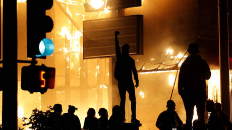 A protester stands on a platform in front of a fire at a restaurant, early Friday, May 29, 2020, in Minneapolis. © AP Photo/Julio Cortez