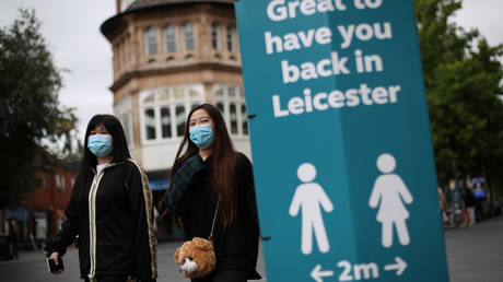 People wearing protective masks walk past a sign, amid the Covid-19 outbreak, in Leicester, Britain, © REUTERS/Carl Recine