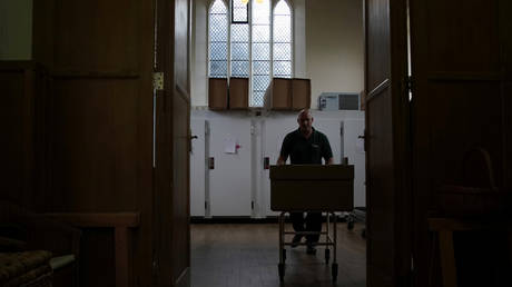 A mortuary worker pushes a coffin containing the body of a deceased man © REUTERS/Hannah McKay