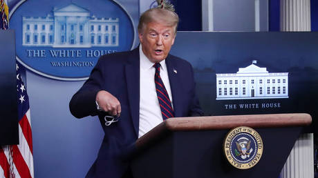 FILE PHOTO: US President Donald Trump pulls a protective face mask from his pocket to show it to reporters at a news briefing at the White House in Washington, DC.