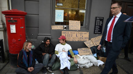 A man walks past the "Homeless Entrepreneur" speaking with a group of other homeless people on the High Street on May 18, 2018