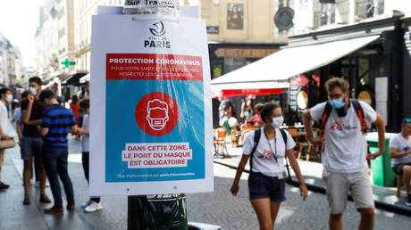 Pedestrians wearing protective face masks walk by a coronavirus disease (COVID-19) information sign in France on August 13, 2020.