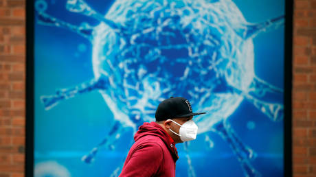 A man wearing a protective face mask walks past an illustration of a virus outside a regional science center in the UK. © REUTERS/Phil Noble/ file photo
