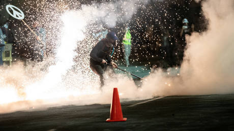 FILE PHOTO: A protester uses a street broom to push away a tear gas canister fired by federal law enforcement officers during a demonstration against police violence in Portland, Oregon.