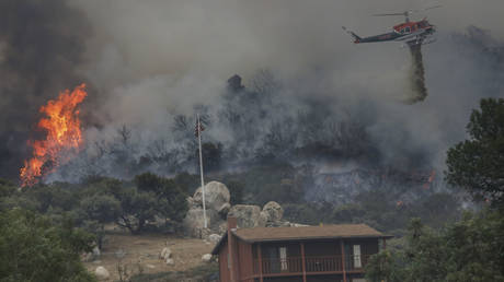 A brush fire encroaches along Japatul Road as a helicopter drops water during the Valley Fire in Jamul, California on September 6, 2020