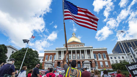 A man with a QAnon vest and US Flag joins hundreds of people of mixed political views, religions and cultures as they protest a mandate from the Massachusetts in Boston on August 30, 2020.