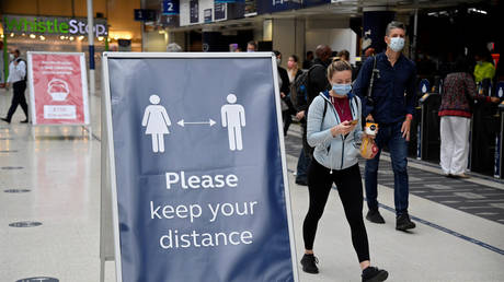 FILE PHOTO: People wearing masks pass a social distancing sign at Waterloo station in London. September 7, 2020. Toby Melville / Reuters