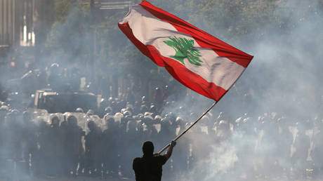 A demonstrator waves the Lebanese flag in front of riot police during a protest in Beirut, Lebanon, August 8, 2020.