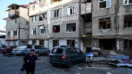 A woman walks front of an apartment building that was by recent shelling Nagorno-Karabakh region's main city of Stepanakert on October 3, 2020. © AFP