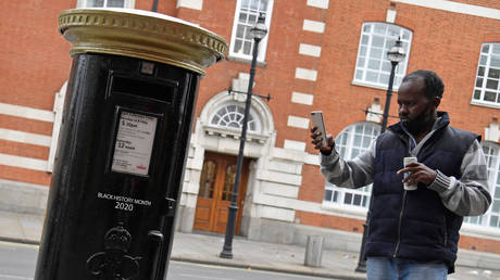 A pedestrian films a Royal Mail postbox, painted black instead of traditional red, to honour Black Britons, as part of the forthcoming Black History Month, in Brixton, London, Britain, September 30, 2020.