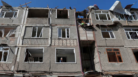 An elderly woman stands on the balcony of an apartment building damaged during the military conflict over the breakaway region of Nagorno-Karabakh, in Stepanakert October 11, 2020.