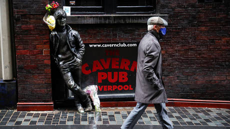 A man wearing a face mask walks past John Lennon statue, Liverpool, Britain, (FILE PHOTO) © REUTERS/Phil Noble
