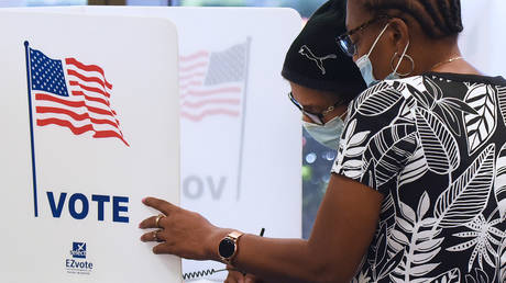 Women wearing face masks fill out vote-by-mail ballots at the Orange County Supervisor of Elections office on October 15, 2020 in Orlando, Florida