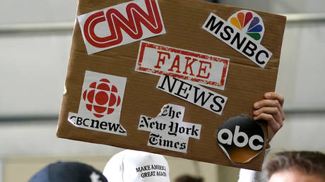 A sign showing major news organizations along with the words "fake news" is held up as US President Donald Trump speaks at a Make America Great Again Rally in Washington, Michigan April 28, 2018.