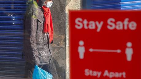 FILE PHOTO: A person wearing a protective mask walks near a social distancing sign in Coventry, Britain.