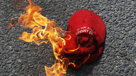 A Make America Great Again hat engulfed in flames burns on the ground after counter protesters lit it on fire in front of the barricade.