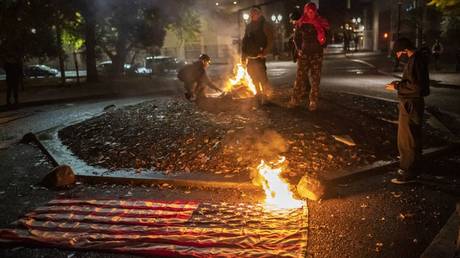 A small group of racial justice protesters watch a burning American Flag as they gather in front of the Multnomah County Justice Center early in the morning on November 4, 2020 in Portland, Oregon