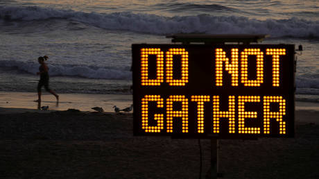 FILE PHOTO: A runner jogs past a public health sign on the beach during the coronavirus outbreak in Oceanside, California.