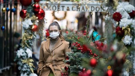 A woman wears a mask as she walks past Christmas-themed window displays in London. November 23, 2020. © AFP / Tolga Akmen