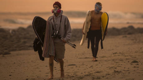 A smoke-filled sky filter orange light around surfers as the Thomas Fire continues to grow and threaten communities from Carpinteria to Santa Barbara on December 12, 2017 in Carpinteria, California.