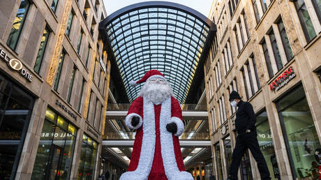 A man walks past a giant Santa Claus figure outside a shopping mall in Berlin. November 2020. © AFP / John MacDougall