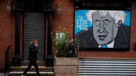 A woman walks past a caricature of Britain's Prime Minister Boris Johnson in the boarded up window of a closed pub in Manchester, Britain, (FILE PHOTO) © REUTERS/Phil Noble