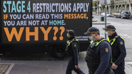 Victorian protective service officers walk past a sign urging people to stay home during Melbourne's lockdown. © AP Photo/Asanka Brendon Ratnayake