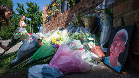 A painted portrait is seen among the flowers as students pay their respects to the murdered school teacher James Furlong outside The Holt School, on June 22, 2020 in Wokingham, England. © Getty Images / Leon Neal