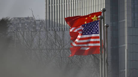 FILE PHOTO: Chinese and US flags at the entrance of an office building in Beijing, January 2020. © Wang Zhao / AFP